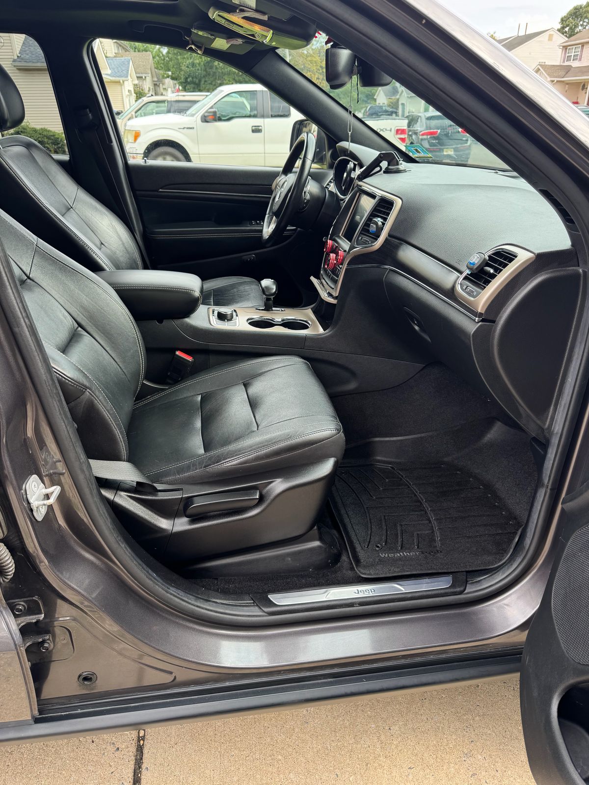 Jeep Grand Cherokee front interior after detailing — black leather seats, clean WeatherTech mat, and a spotless cabin.